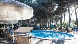 Una piscina con sillas de descanso y una sombrilla de paja.