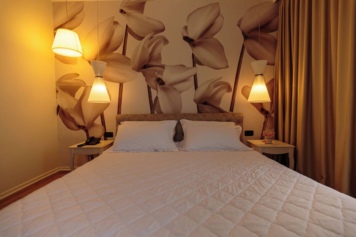 A hotel room with a large bed, two bedside tables, and a wall with a floral pattern.
