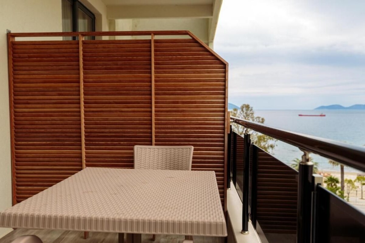 A balcony with a table and chair, a wooden partition, and a view of the sea.
