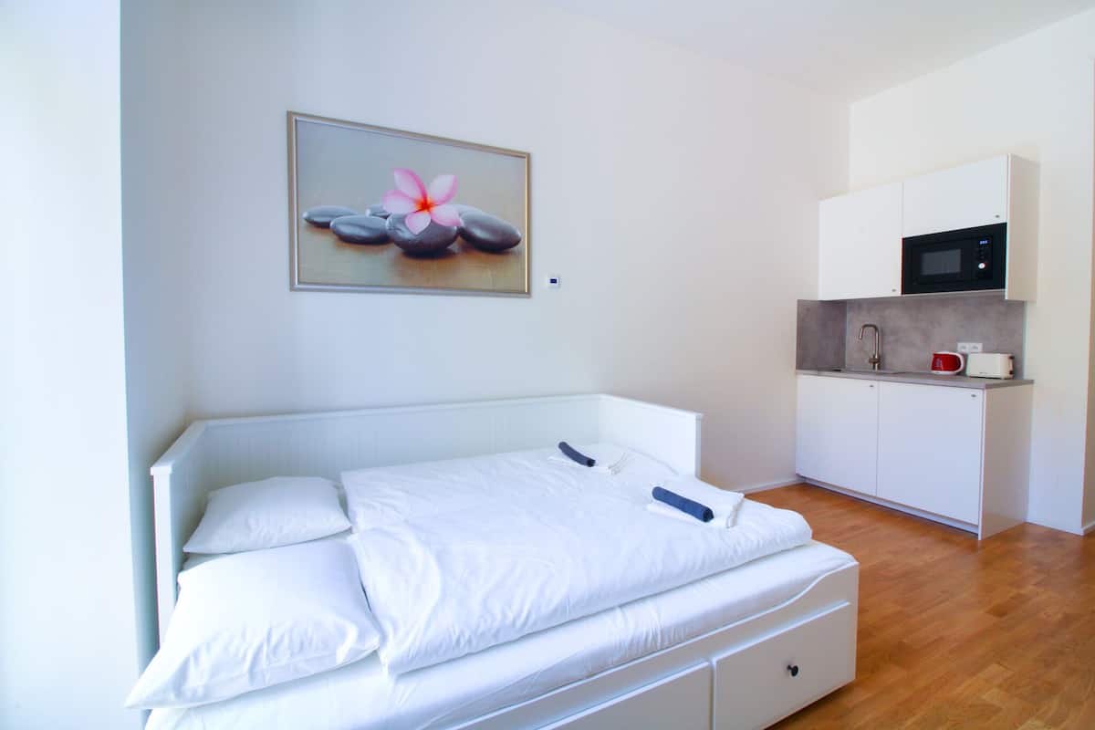 Un dormitorio con cama, una kitchenette pequeña y un cuadro colgado en la pared.