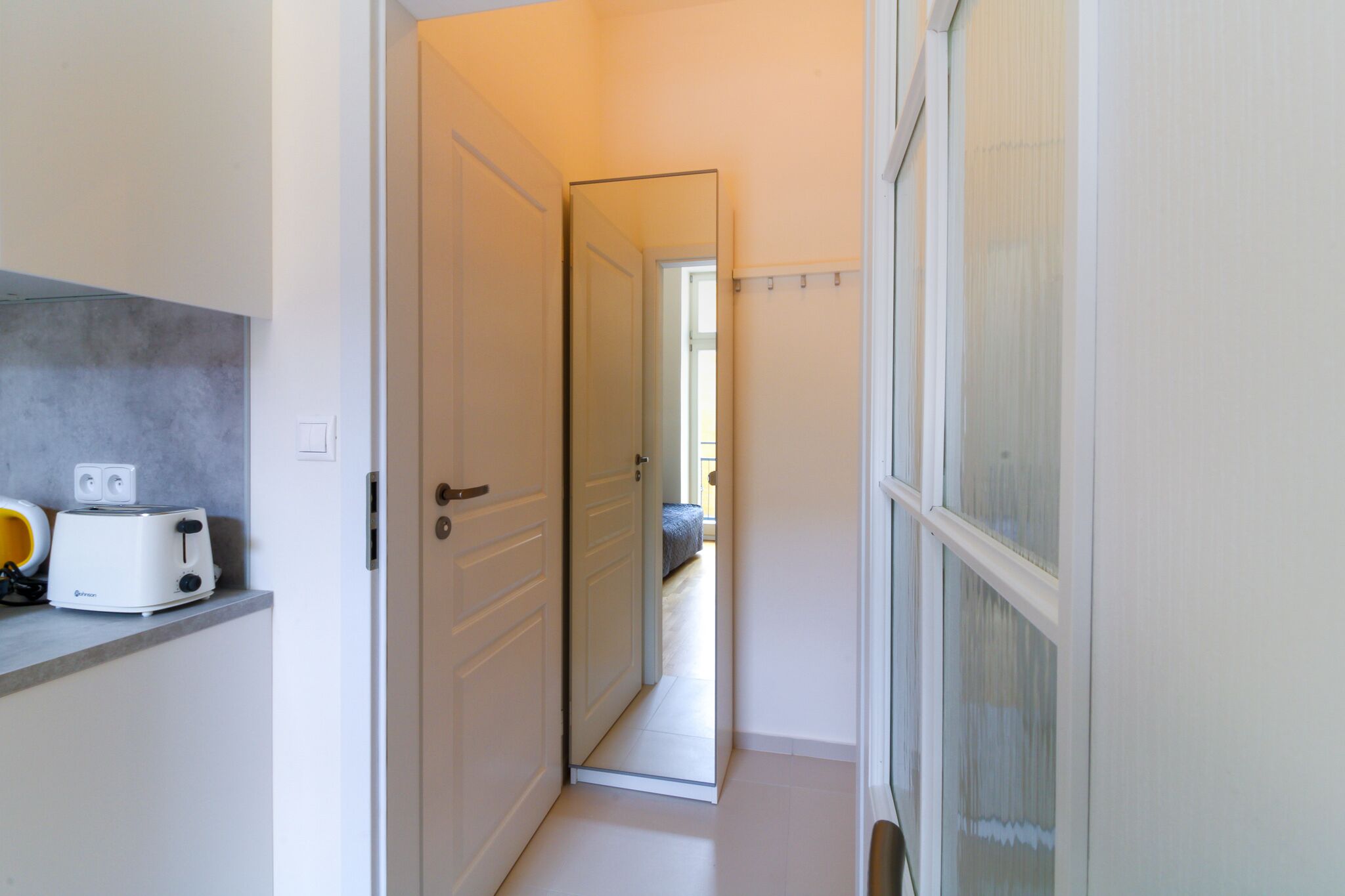 Un corridoio stretto con una zona cucina a sinistra, una porta che dà su un'altra stanza e una finestra a destra.