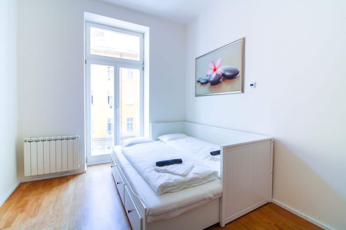 Un dormitorio con cama, radiador, ventana y un cuadro en la pared.