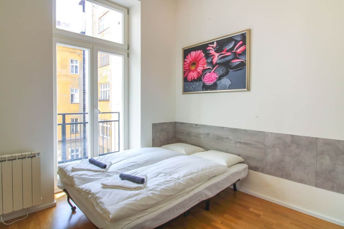 Un dormitorio con cama, radiador, ventana y un cuadro en la pared.