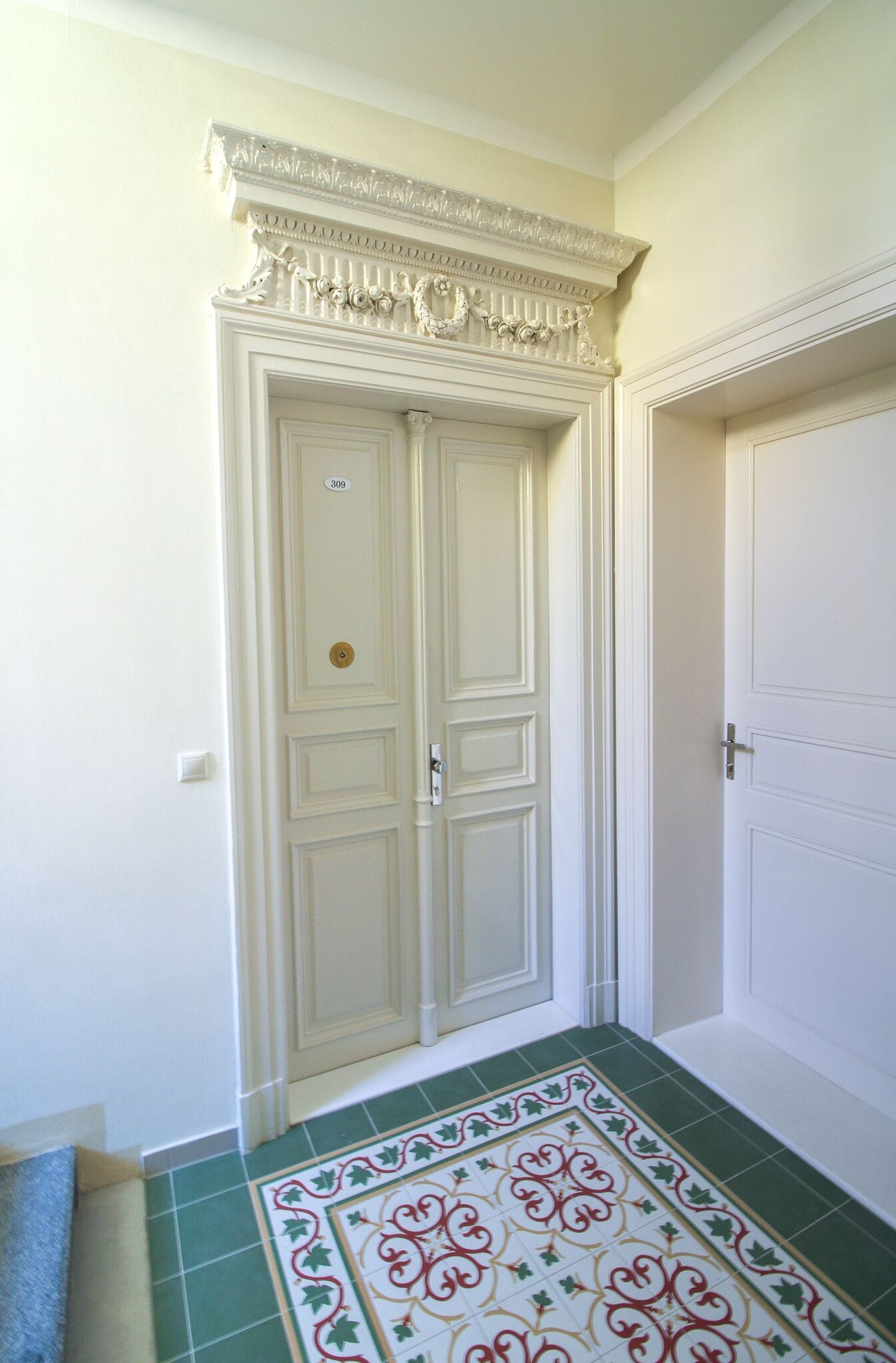 A white double door with a decorative molding above it, a green and white patterned floor, and a small towel on the floor to the left.