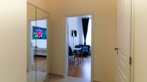 Un couloir mène à une chambre à coucher avec un lit, à un coin repas avec une table et des chaises, et à un salon avec un canapé et un téléviseur.