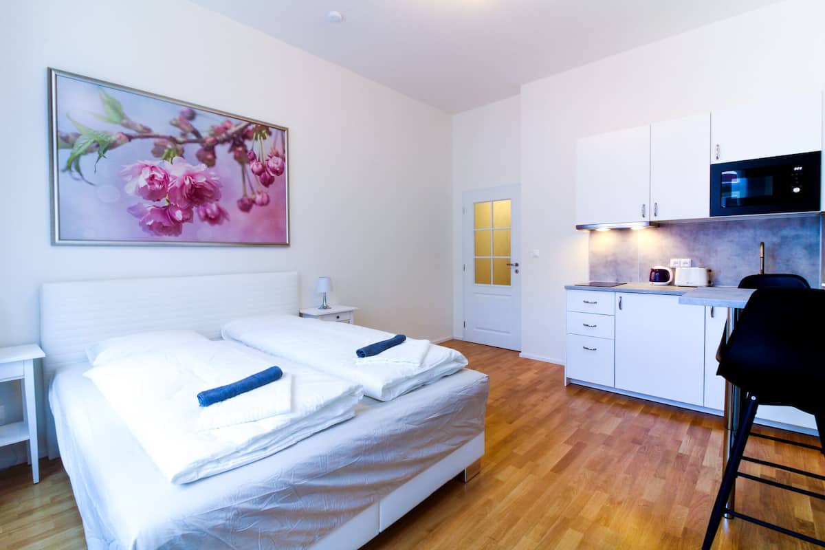 Una habitación de hotel moderna con una cama, una mesita de noche pequeña, una cocina con microondas y una puerta con luz.