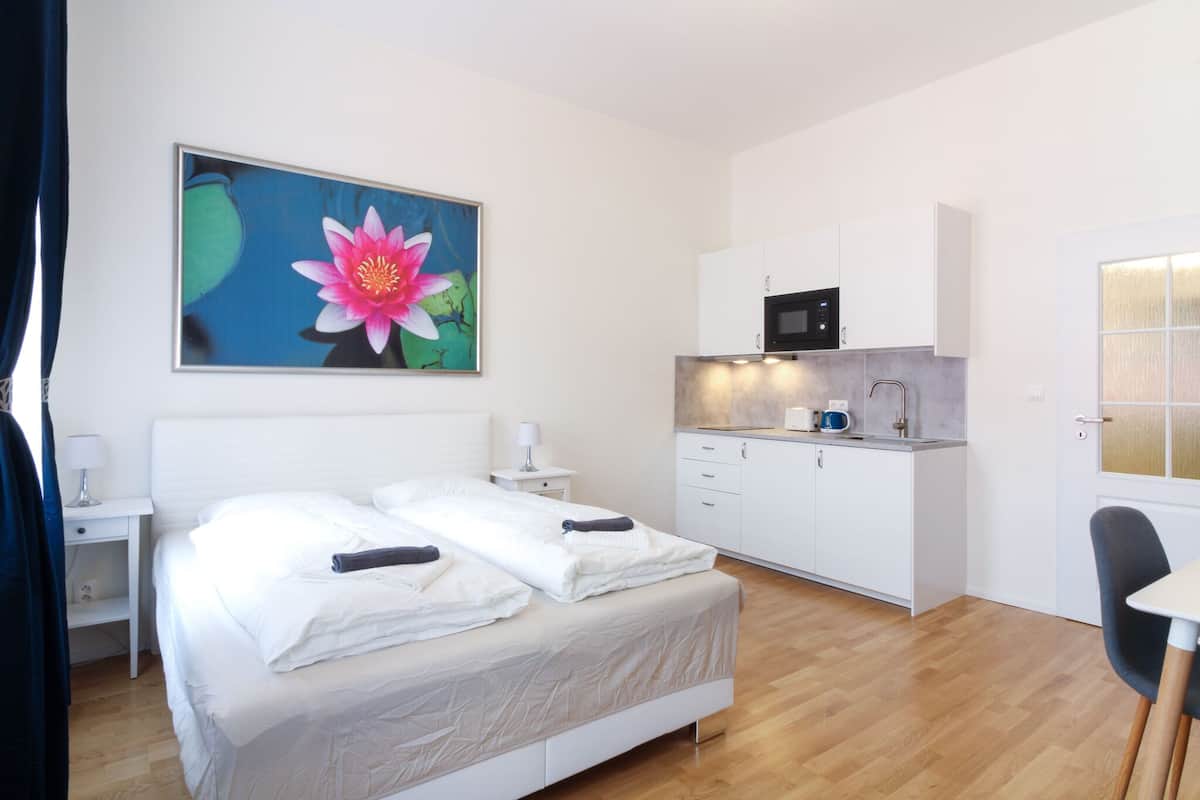 Una habitación de hotel moderna con una cama bien hecha, una kitchenette pequeña y un ventanal grande.
