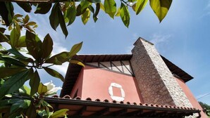 A building with a stone chimney, a red facade, and a tiled roof. - Hotel Rural Porrua (Llanes)