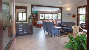 A spacious living area with a sofa, chairs, a dining table, and a kitchen area with cabinets and a window. - Hotel Rural Porrua (Llanes)