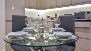 A modern dining area with a glass table surrounded by chairs, plates, and wine glasses. - Silbury MK City Apartment With Parking (Milton Keynes)