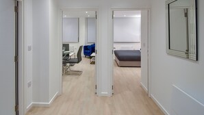 A modern hotel room with a bed, a desk, and a chair. There is a large mirror on the wall and a door leading to another room. - Silbury MK City Apartment With Parking (Milton Keynes)