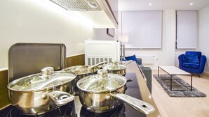 A modern kitchen with stainless steel appliances, a dining area with a blue chair, and a view of the city through large windows. - Silbury MK City Apartment With Parking (Milton Keynes)