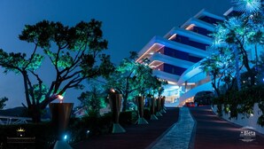 Ein modernes Hotel mit einzigartigem architektonischen Design, das sich durch eine mehrstöckige Struktur und einen von Bäumen und Zierelementen gesäumten Weg auszeichnet.