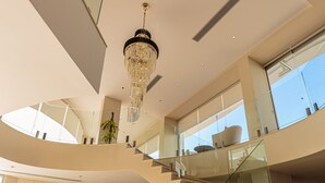Ein geräumiger, mehrstöckiger Innenraum mit moderner Treppe, Glasgeländern und einem Chandelier.
