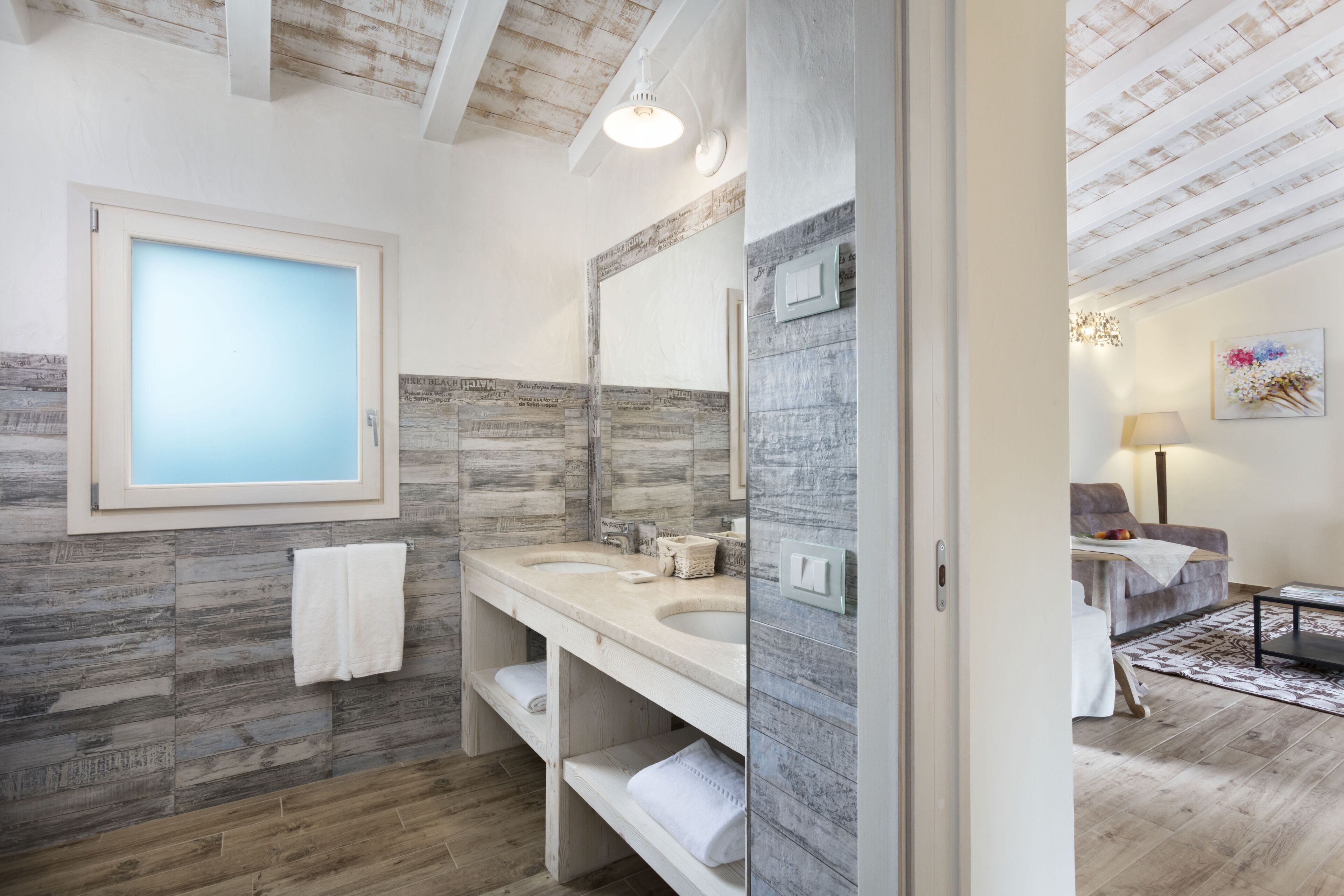 Ein modernes Badezimmer mit Holzboden, einem großen Spiegel, zwei Waschbecken und einem Handtuchhalter.