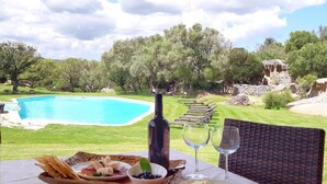 Mesa de jantar com vista para uma piscina, área de estar ao ar livre e uma garrafa de vinho.