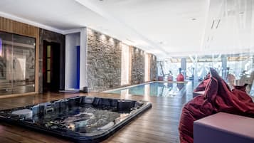 A modern spa area with a hot tub, wooden flooring, stone walls, and a glass-enclosed pool.