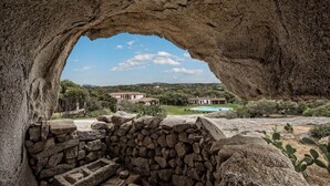Vista através da entrada de uma caverna para uma propriedade com piscina e casas ao fundo.