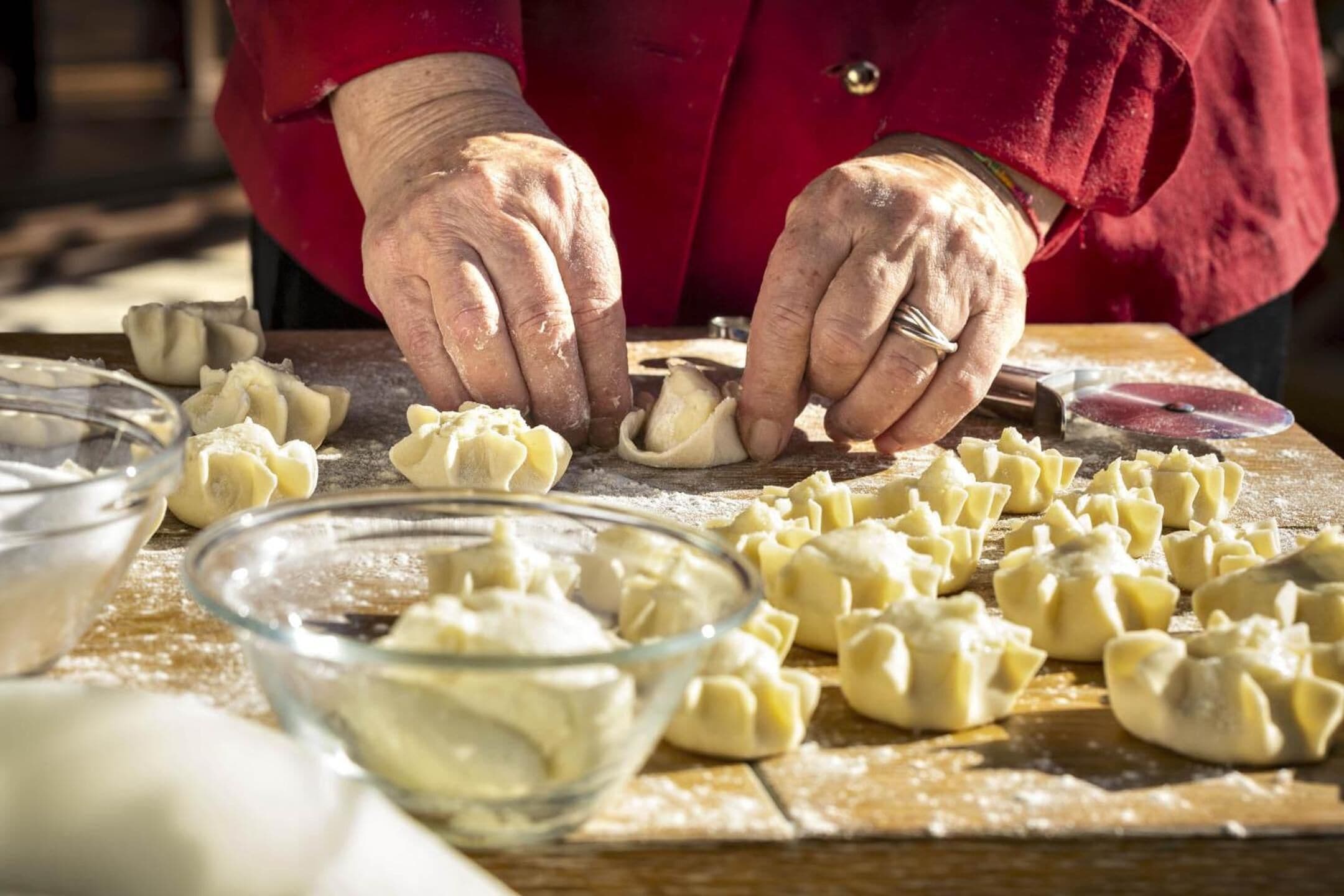 A person preparing dumplings on a wooden table with flour scattered around.