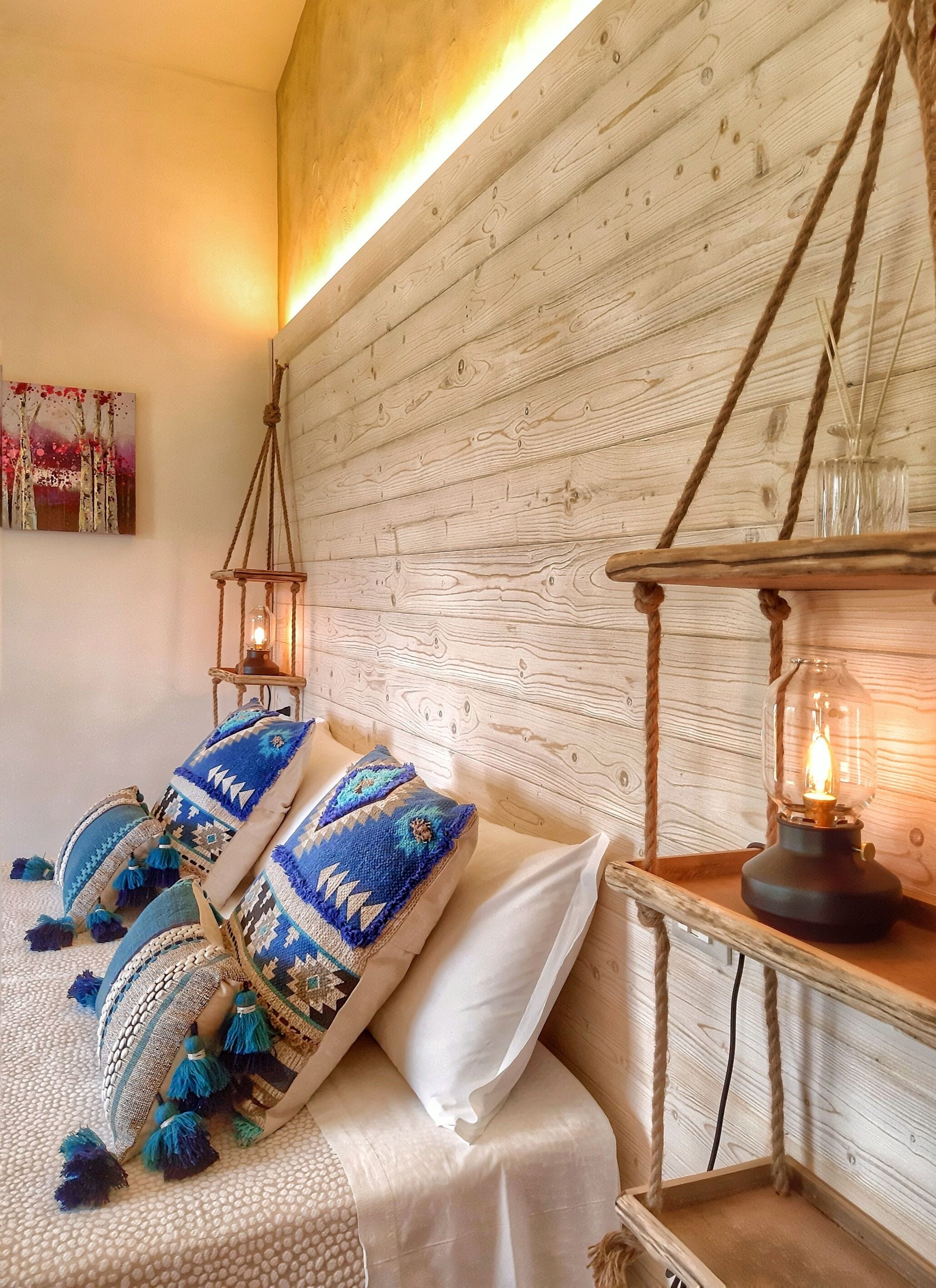 Une chambre chaleureuse avec une tête de lit en bois, un lit agrémenté d’oreillers à motifs bleus et blancs, et une lanterne suspendue.