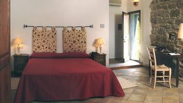 A bedroom with a large bed, two nightstands, a chair, and a stone wall.