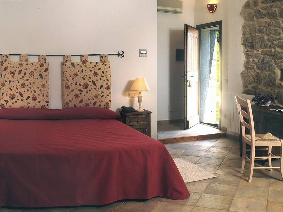 A bedroom with a large bed, two nightstands, a chair, and a stone wall.