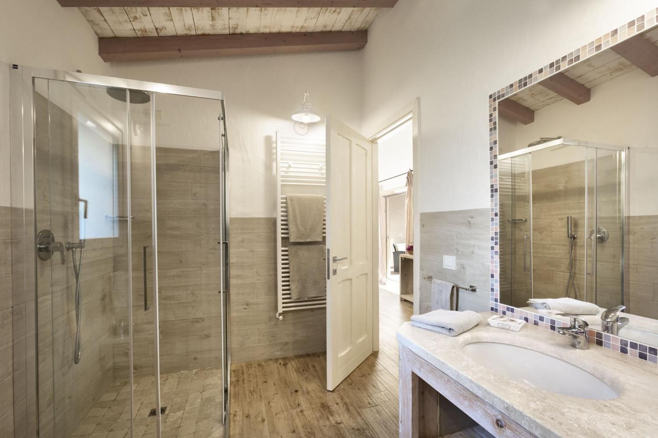 Un bagno moderno con cabina doccia in vetro, uno specchio grande e un pavimento in legno.