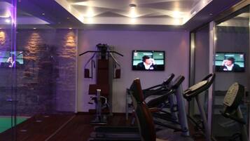 Ein Fitnessraum mit Trainingsgeräten, einer Steinwand und zwei an der Wand befestigten Fernsehgeräten.