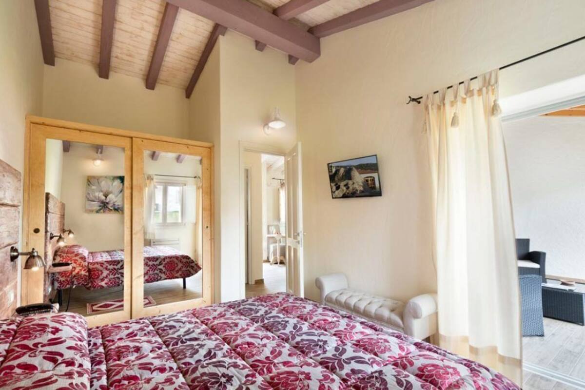 A bedroom with a large bed, a sitting area with chairs, a balcony with a view, and a door leading to another room.