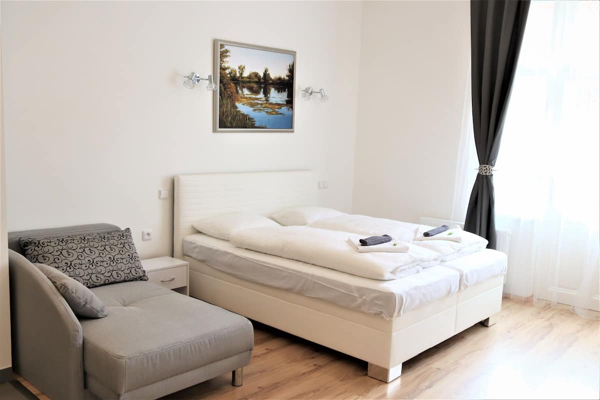 A bedroom with a bed, a nightstand, a chair, and a wall-mounted picture.