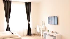 A modern hotel room with a bed, a desk, a chair, and a TV on the wall. - Flowers apartments (Prague)