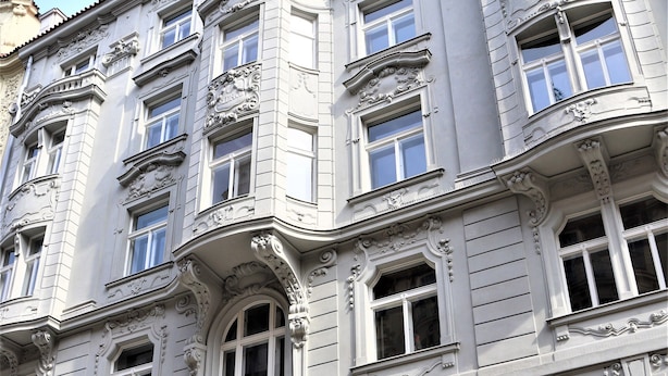 A multi-story building with ornate architectural details, large windows, and a prominent entrance with a wooden door. - Flowers apartments (Prague)