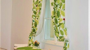 A small dining area with a table and two chairs, a radiator below the window, and a curtain with a leaf pattern. - Reznicka Apartments (Prague)
