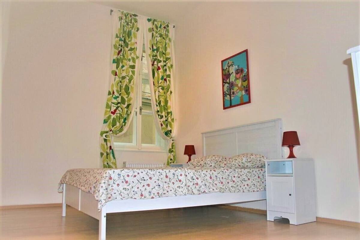 Une chambre à coucher avec un lit, des tables de chevet, une fenêtre avec des rideaux et un tableau accroché au mur.