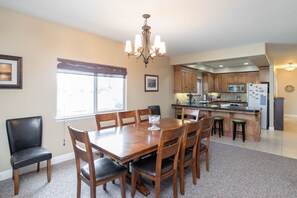 A dining area with a wooden table and chairs, a chandelier, and a kitchen in the background. - *Shellebration! HUGE Beach House, Steps from the Sand! Perfect for Any Family Getaways!* (Oceano)