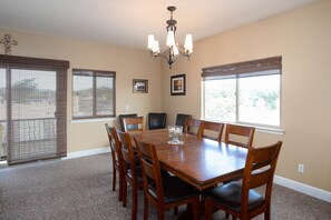 A dining room with a wooden table and chairs, a chandelier, and large windows with blinds. - *Shellebration! HUGE Beach House, Steps from the Sand! Perfect for Any Family Getaways!* (Oceano)