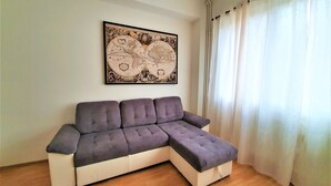 A living room with a sectional sofa, a world map artwork on the wall, and a window with curtains. - Epstein Apartments (Prague)