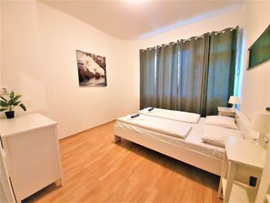 Quarto com cama, mesa de cabeceira, abajur, planta em vaso e quadro na parede.