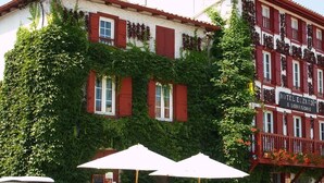 Un edificio con contraventanas rojas, un balcón adornado con flores y un letrero que dice "HOTEL EL ZKAD".