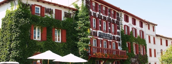 A building with red shutters, a balcony with flowers, and a sign that reads "HOTEL EL ZKAD".