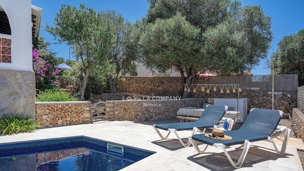 Piscina com espreguiçadeiras, parede de pedra e pérgola com luzes penduradas.