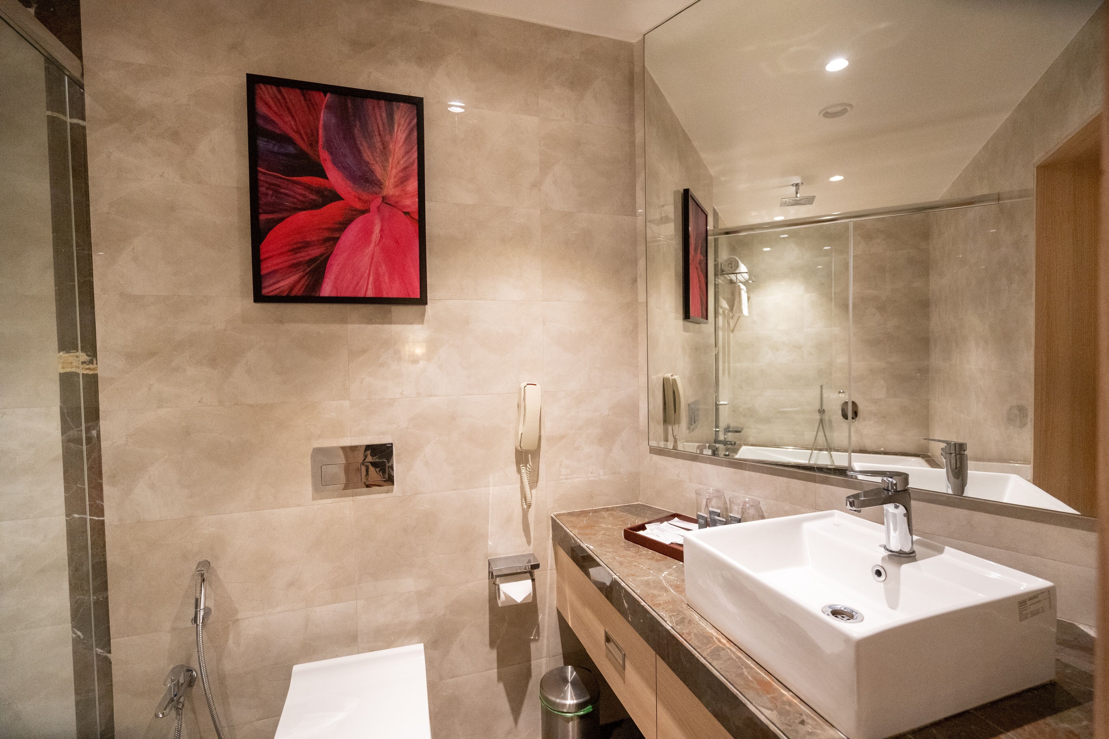 A modern bathroom with a large mirror, two sinks, a shower, and a toilet.