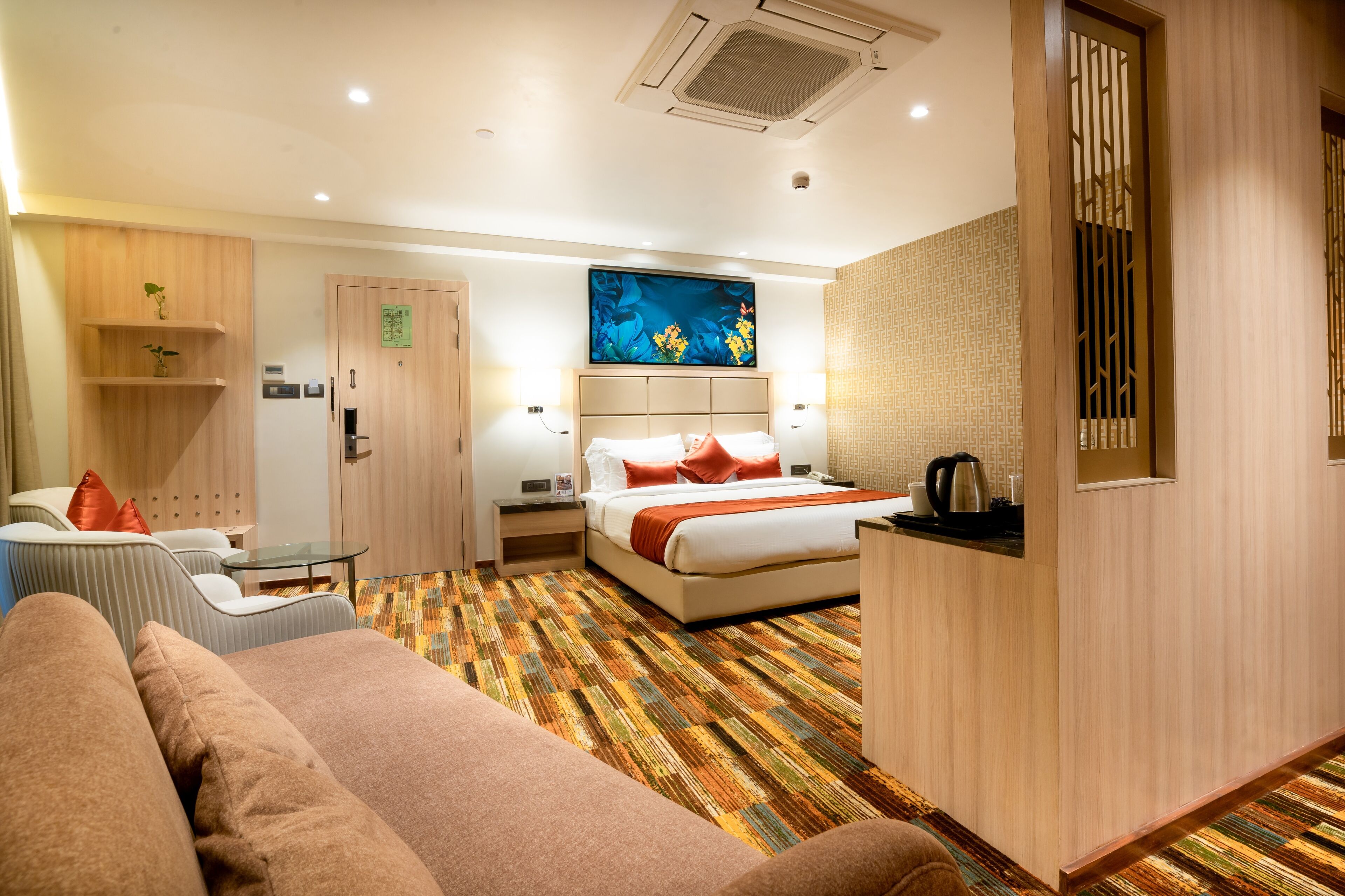 A hotel room with a bed, a sofa, a desk, and a wall-mounted TV.