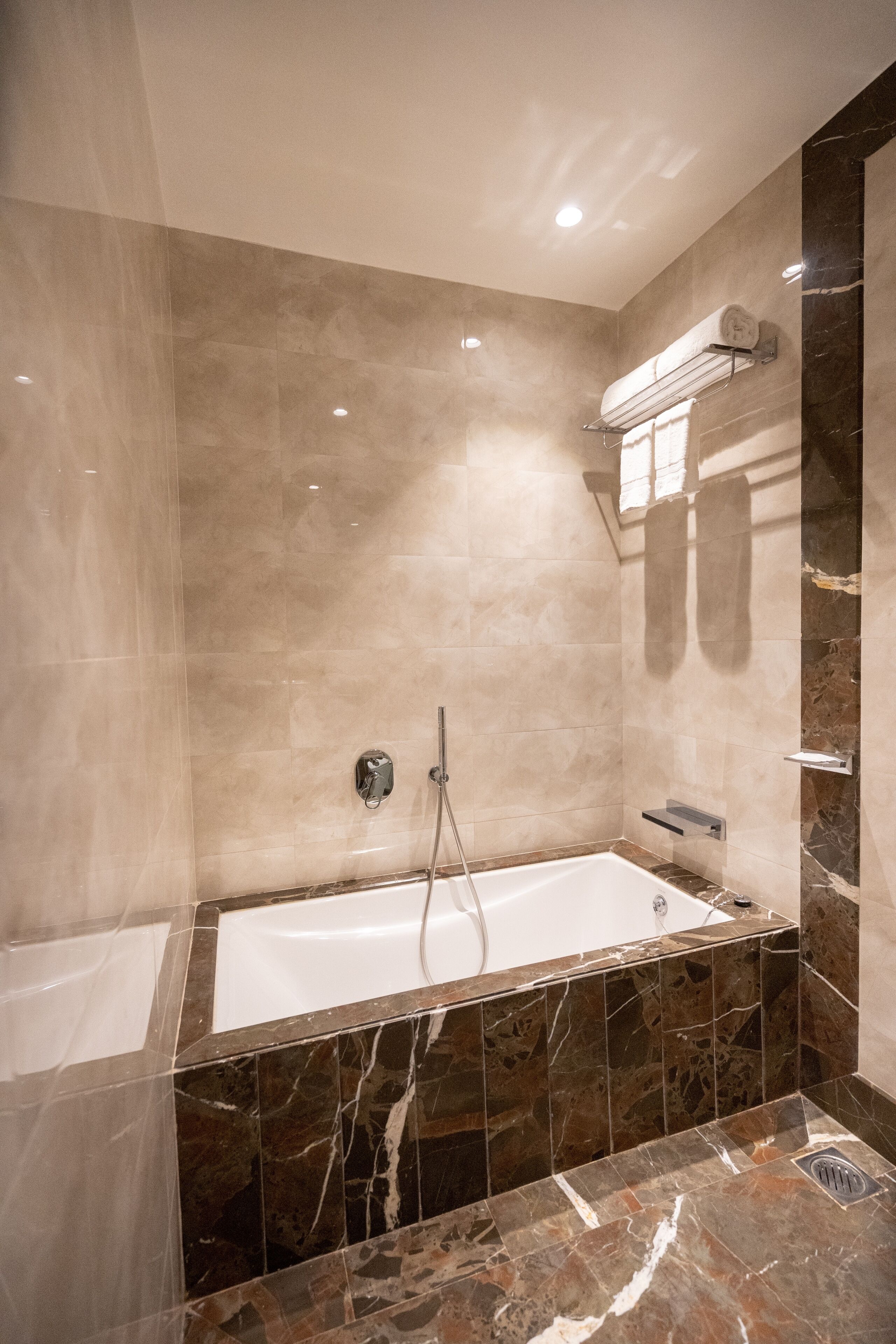 A modern bathroom with a bathtub, a shower, and a towel rack.