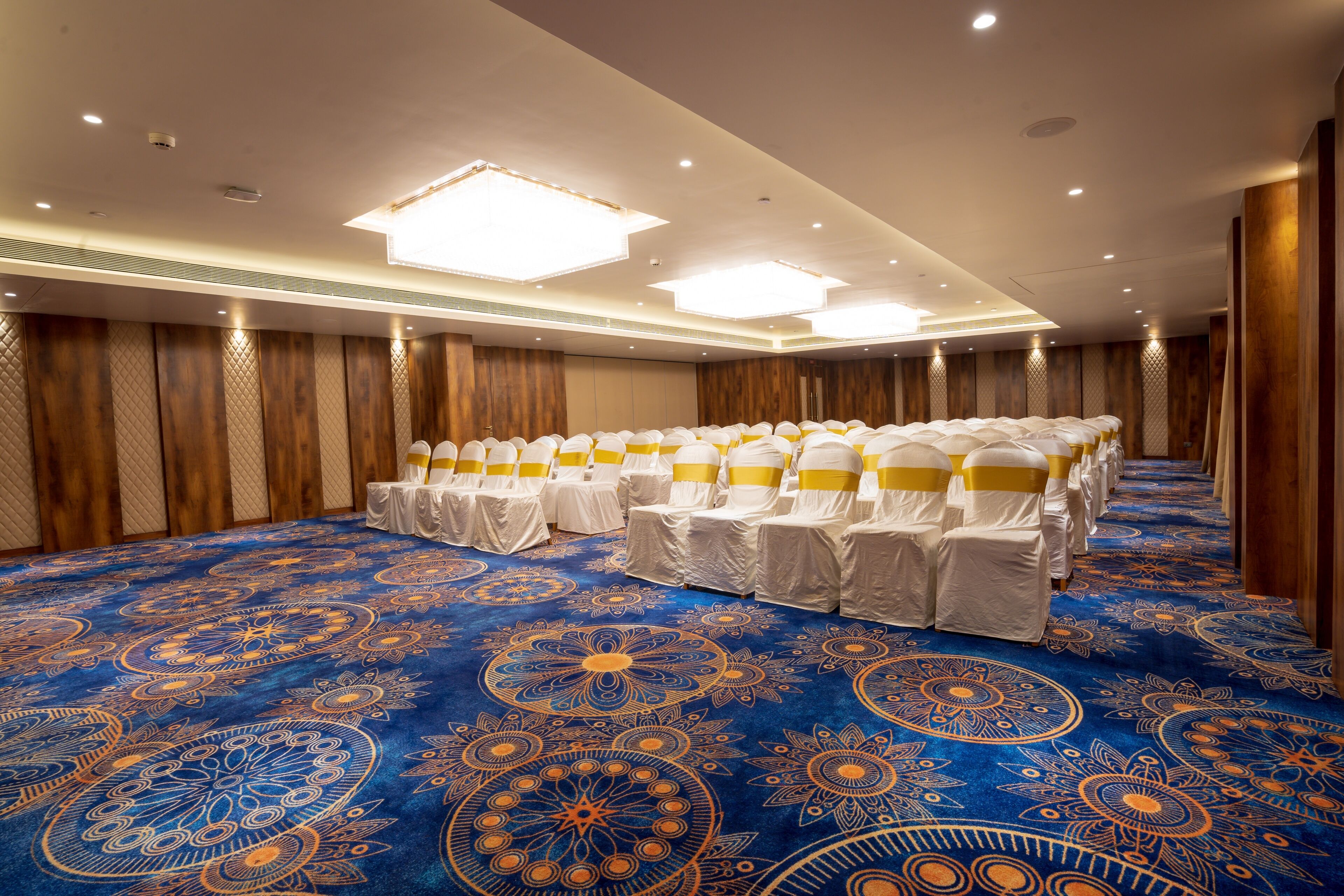 A conference room with rows of white chairs, each with a yellow sash, on a blue patterned carpet.