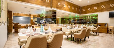 Un comedor amplio con varias mesas y sillas, paneles de madera en las paredes y una lámpara moderna.