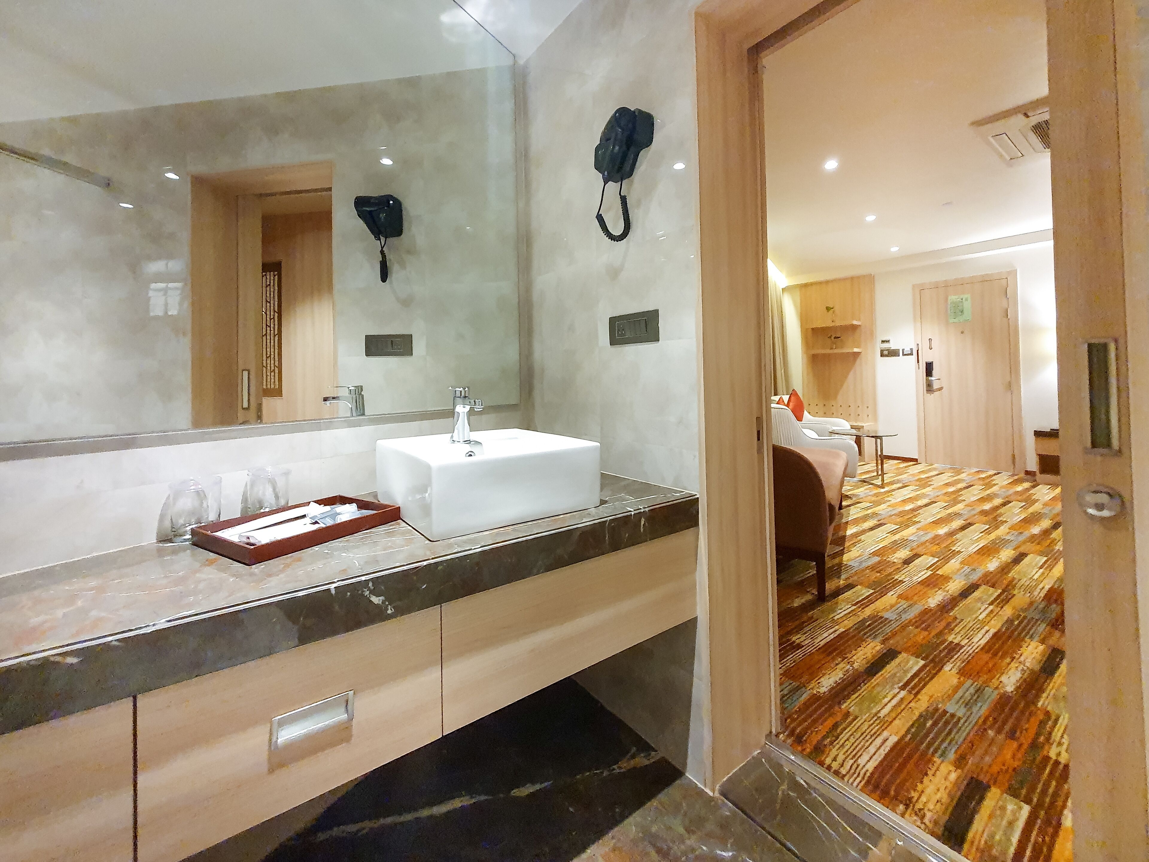 A hotel bathroom with a large mirror, a white sink, and a telephone.