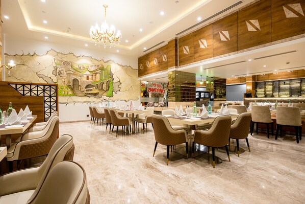 Un restaurante con suelo de mármol, paredes de paneles de madera y un mural con un paisaje. Las mesas están dispuestas con sillas y servilletas.