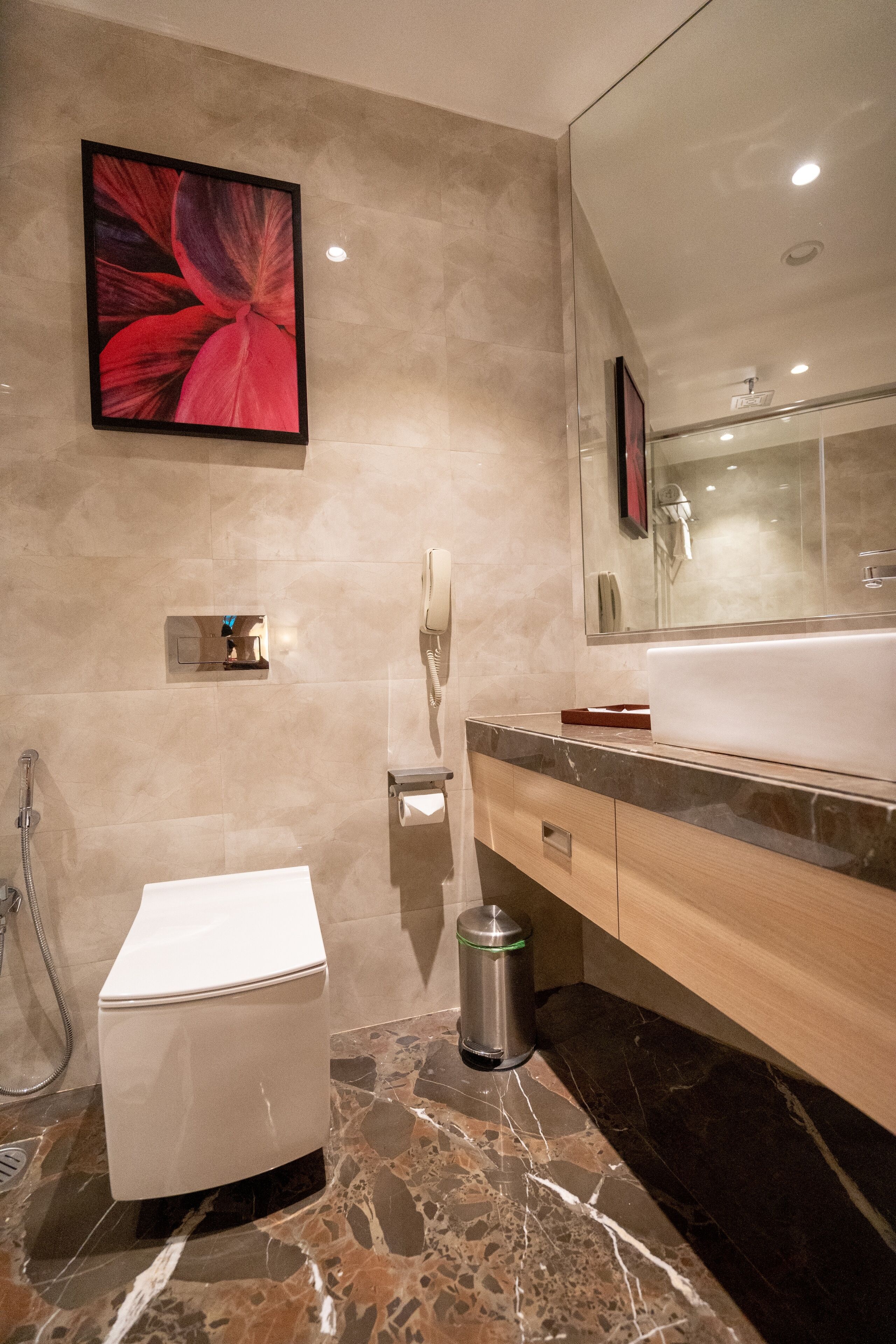 Une salle de bain moderne avec un grand miroir, des toilettes blanches, un lavabo et une poubelle.