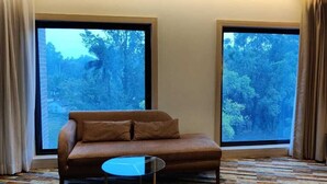 Una habitación con sofá, una pequeña mesa redonda y ventanas amplias con vistas a un bosque.